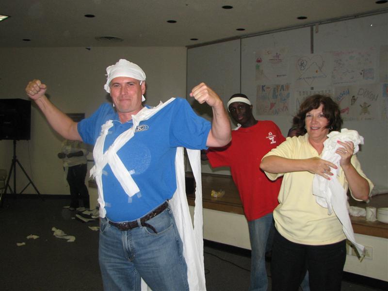 IMG_0480.JPG - Skit time!  What could you and five others think of to use ten rolls of toilet paper?  Why you dress up Governor Designate Tom Ganse as “The Man Who Wear’s the K”, with muscles!  You had to be there.  Next year, you should be!